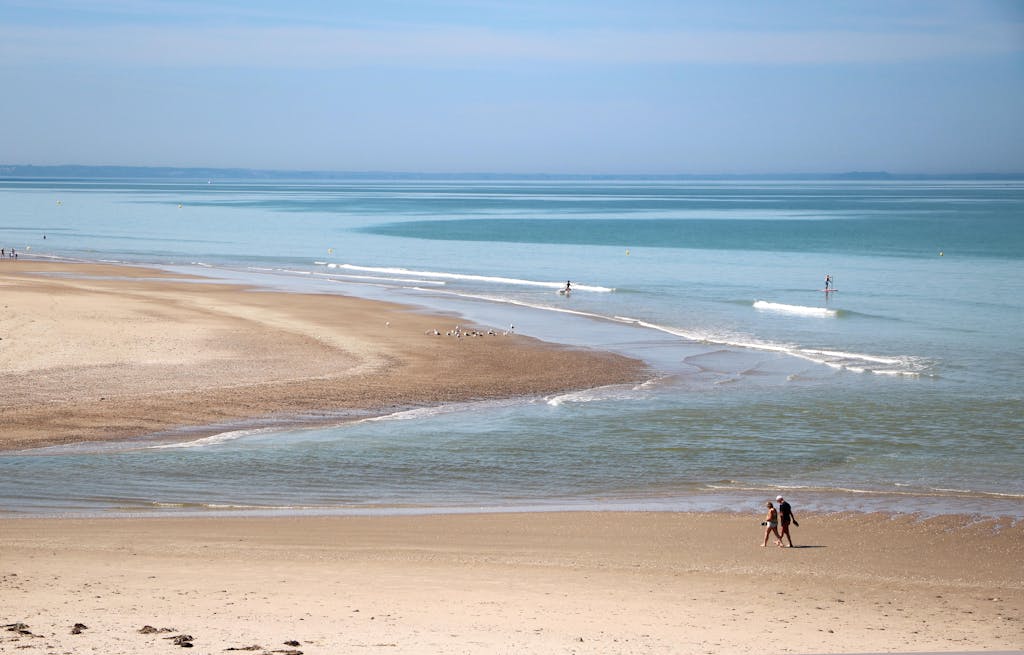 Peaceful beach scene in Saint-Pair-sur-Mer, Normandie, France with tourists strolling along the shore.